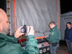 A NAV szakemberei plombát raknak egy Ukrajna felől érkezett tranzitkamionra, miután mintát vettek a Nemzeti Élelmiszerlánc-biztonsági Hivatal (Nébih) szakemberei a jármű kukoricaszállítmányából a záhonyi közúti határátkelőhelyen 2023. április 17-én késő este. Jobbra, Nobilis Márton, az Agrárminisztérium élelmiszeriparért és kereskedelempolitikáért felelős államtitkára.